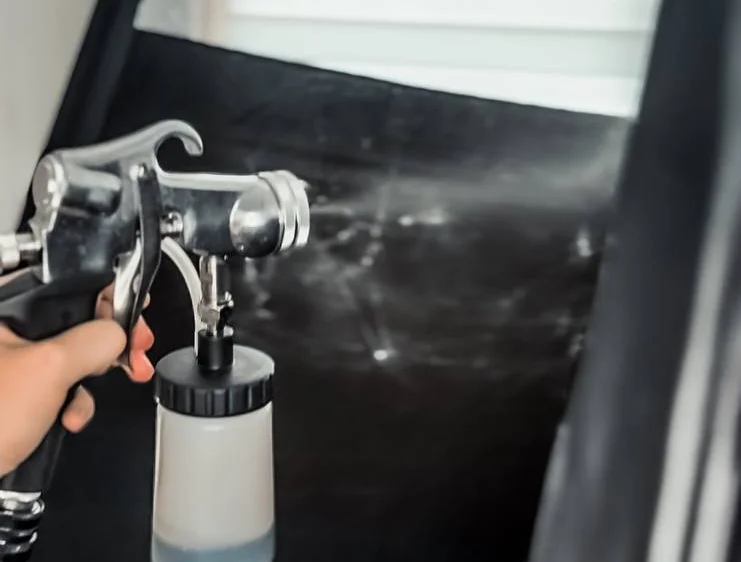 A professional spray tan gun in action inside a tanning booth.